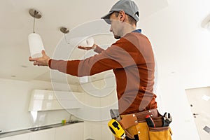 Electrician in uniform repairing ceiling lamp indoors