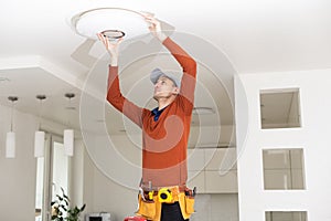 Electrician in uniform repairing ceiling lamp indoors