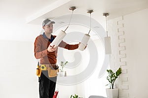 Electrician in uniform repairing ceiling lamp indoors