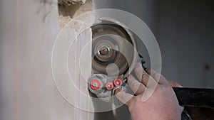 An electrician uses a grinder to drill a hole in the wall for laying an electric cable
