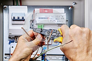 An electrician uses stripper cutter tool to remove insulation from ends of wires when connecting power cable to