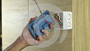 Electrician is using a screwdriver to tighten the wires to the electrical plug on a wooden wall.