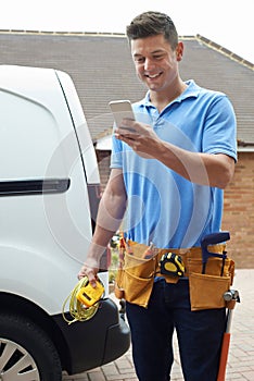 Electrician With Van Texting On Mobile Phone Outside House photo