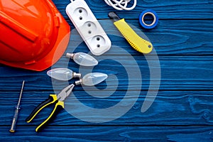 Electrician work concept. Hard hat, tools, bulb, socket outlet on blue wooden background top view copy space