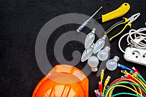 Electrician work concept. Hard hat, tools, cabel, bulb, socket outlet on black background top view space for text