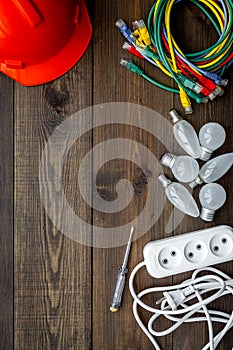 Electrician work concept. Hard hat, tools, cabel, bulb, socket outlet on dark wooden background top view space for text