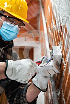 Electrician at work with face protected by surgical mask to prevent Coronavirus infection. Covid-19 Pandemic Prevention