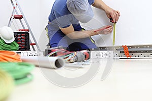 Electrician at work with pencil and meter measures on the wall the position for the electric socket, install electric circuits,