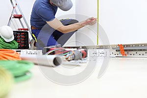 Electrician at work with pencil and meter measures on the wall the position for the electric socket, install electric circuits,