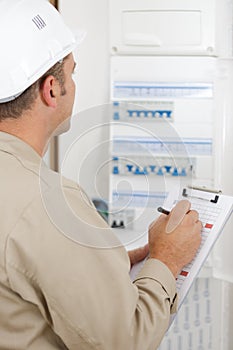Electrician worker checking clipboard while working in fuse-board