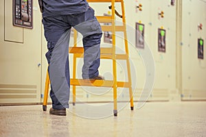 Electrician worker with wooden ladder on electrical cabinets background