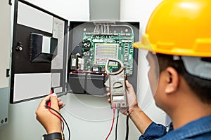 Electrician working use digital clamp meter in hands of electrician, close-up against background of electrical wires and relays.