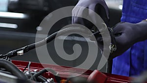 Electrician works with electric block in car. Close-up of automobile inside under raised hood. Service man hands working