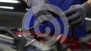 Electrician works with electric block in car. Close-up of automobile inside under raised hood. Service man hands working