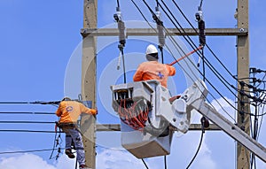 Electricians with articulated boom lift working to install electrical transmission on power pole against blue sky