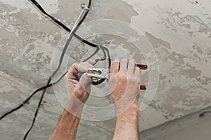 Electricians cleans the contacts with pliers. Installing the ceiling light