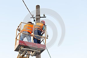Electricians on the pillars install the mount for the power line. Professional electricians work on the tower