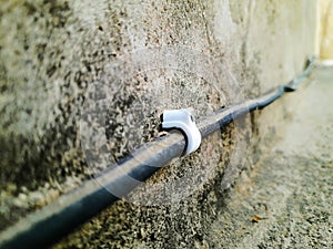 An electricity cable fitted on a rusty old wall in a small factory with the help of plastic holding clips with iron nail