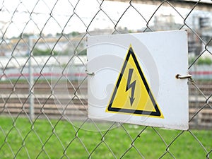 Electricity caution sign on trellised fence, on blurred city background, danger sign