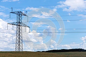 Electricity concept. High voltage power line pylons, electrical tower on a green field with blue sky