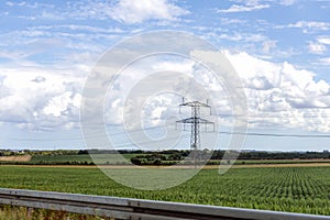 Electricity concept. High voltage power line pylons, electrical tower on a green field with blue sky