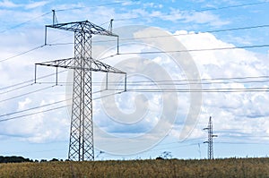 Electricity concept. High voltage power line pylons, electrical tower on a green field with blue sky.