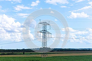 Electricity concept. High voltage power line pylons, electrical tower on a green field with blue sky.