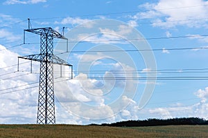 Electricity concept. High voltage power line pylons, electrical tower on a green field with blue sky.