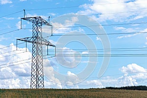 Electricity concept. High voltage power line pylons, electrical tower on a green field with blue sky.