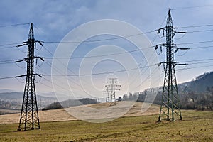 Electricity conduction cables on metal frame transmission towers leading to a small Czech town in background