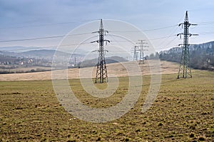 Electricity conduction cables on metal frame transmission towers leading to a small Czech town in background