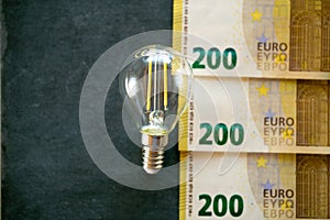 Electricity cost. Light bulb, euro banknotes and coins on black chalk board.Increasing the cost of light and heat.Rising