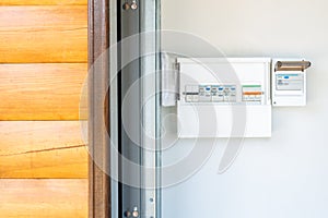 Electricity distribution board with set of automatic circuit breakers and switches near entrance door of wooden garage building.