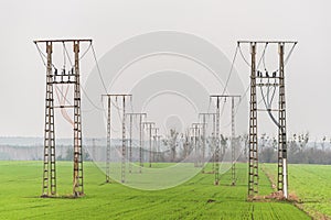 Electricity distribution system. Two-track high voltage overhead power line, power pylon, steel lattice tower standing on field