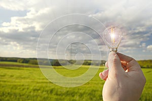 Electricity and green energy.Light bulb in hand on electricity power line background. Power lines on blue sky and green