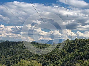 Electricity infrastructure. power lines across mountains landscape, blue sky, green fields and path. Energy industry. Copy space