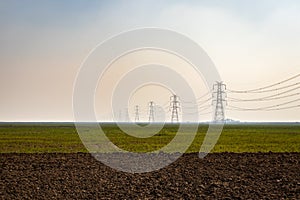 electricity pole with high tension power transmission cable in green fields