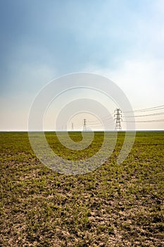 Electricity pole with high tension power transmission cable in green fields of countryside area