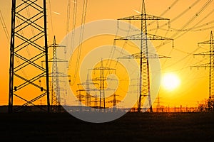 Electricity poles and electric power transmission lines against vibrant orange sky at sunset on a hot day with flickering air.