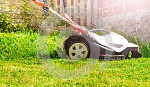 Electricity powered lawnmower cutting fresh grass on lawn