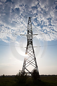 Electricity pylon against the cloudy sky and the shining sun