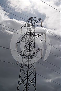 An electricity pylon against a dark cloudy sky. Sunlit insulators.