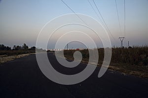 Electricity pylon in a field behind an embankment at the edge of a country road at sunset