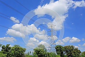 Electricity pylon of high-voltage power lines on green field with beautiful clouds on blue sky