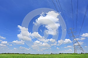 Electricity pylon of high-voltage power lines on green field with beautiful clouds on blue sky. Perspective and Landscape view