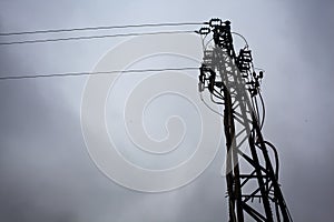 Electricity pylon with over head cables passing on it and a cloudy sky as background