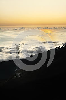 Electricity pylon over valley at sunset