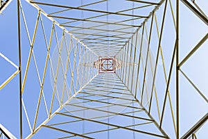 Electricity pylon in perspective seen from below with blue sky background