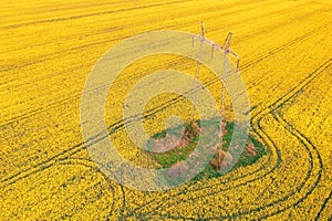 Electricity pylon and power lines over blooming rapeseed crops field, aerial view drone pov