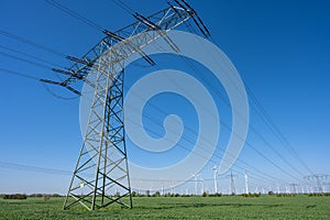 An electricity pylon with power lines and wind turbines